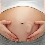 Brzuszek w 30 tygodniu ciąży, z widocznym odciskiem stópki dziecka. Ręce mamy delikatnie obejmują rosnący brzuch.