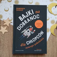Książka "Bajki na dobranoc dla chłopców nowego pokolenia" z rakietą na okładce, otoczona złotymi gwiazdkami i księżycami.