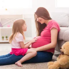 Córka z czułością dotyka brzucha mamy, która wyjaśnia jej, jak wytłumaczyć 10 latkowi skąd się biorą dzieci. Miś czeka na nowego członka rodziny.