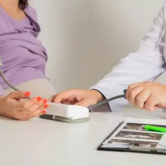 Lekarz mierzy ciśnienie pacjentce, która jest w ciąży. Na biurku leżą zdjęcia USG, co sugeruje stan przedrzucawkowy.