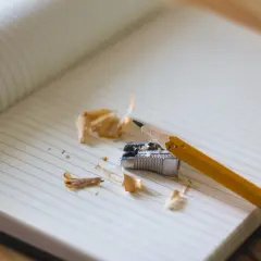 Ołówek i temperówka na kartce w kratkę. Wokół resztki drewna i papieru. Może to symbolizować trudności w nauce i nieklasyfikowanie ucznia.
