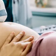 Lekarz wykonuje usg połówkowe, przykładając sondę do brzucha ciężarnej. Widoczny żel i dłoń kobiety.