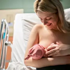 Uśmiechnięta mama karmi piersią noworodka w szpitalu. Choć nie widać tego bezpośrednio, może to być moment, gdy pojawia się grzybica sutka, wymagająca uwagi.