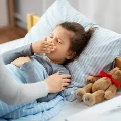 Chora dziewczynka w łóżku, zakrywająca usta. Obok pluszowy miś. Ile dni trwa opieka na dziecko?