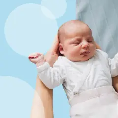 Noworodek śpi w ramionach mamy, jego rączki lekko uniesione, jakby w odruchu Moro.