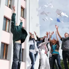 Radosna młodzież rzuca papierami w powietrze, świętując koniec roku szkolnego, kiedy jest wystawienie ocen.