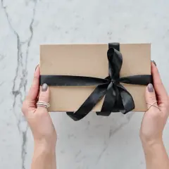 Dzień brata! Elegancki prezent w brązowym pudełku, przewiązany czarną wstążką, trzymany w dłoniach z biżuterią.