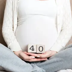 Ciąża trwa 40 tygodni. Kobieta w ciąży trzyma w dłoniach kostki z cyframi 4 i 0.
