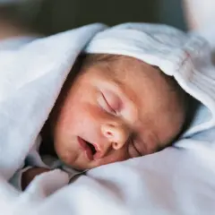 Śpiące niemowlę otulone kocykiem, z czapką na głowie. Może to być mały Ołeksandr lub Sofia, piękne ukraińskie imiona.
