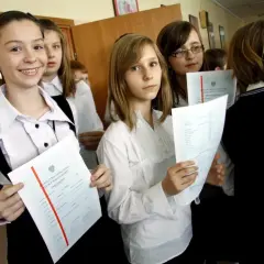 Uczennice z dyplomami, jedna z nich uśmiecha się, zastanawiając się, jaka średnia na czerwony pasek w 4 klasie.