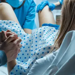 Wsparcie bliskiej osoby podczas porodu. Kobieta trzyma dłoń partnera, otoczona personelem medycznym. To nie jest balonik do porodu, lecz chwila narodzin.