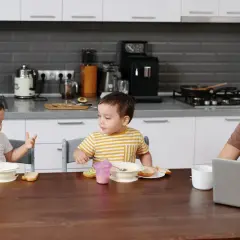 Mama rozmawia z dziećmi przy stole, gdy dziecko zaczyna mówić, gestykulując.