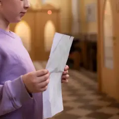 Młoda osoba w fioletowej bluzie trzyma kartkę, przygotowując się do spowiedzi świętej w kościele.