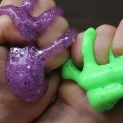 Dzieci bawią się fioletowym i zielonym slime'em, pokazując, jak zrobić slime.
