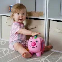 Uśmiechnięta dziewczynka bawi się skarbonką-świnką. To idealny prezent, czyli becikowe dla kogoś, kto dopiero zaczyna oszczędzać.