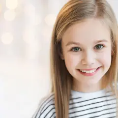 Uśmiechnięta dziewczynka o blond włosach, jakby inspirowana nowoczesnymi imionami dla dziewczyn, z rozmazanym tłem pełnym świateł.