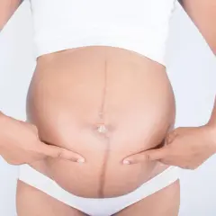 Brzuch kobiety w ciąży z widoczną ciemną linią, linea negra, podkreśloną palcami.