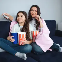 Mama i córka oglądają filmy dla nastolatków, zajadając popcorn i popijając napoje.