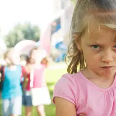 Zagniewana dziewczynka, bunt 7 latka, na tle bawiących się dzieci i placu zabaw.
