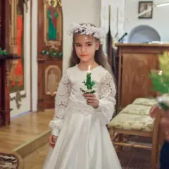 Dziewczynka w białej sukni i wianku trzyma świecę. To ważny dzień, w której klasie komunia.