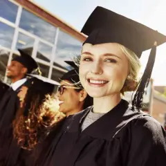 Uśmiechnięta absolwentka w togach i birecie, obok innych studentów. To symbol końca nauki i wyboru nowych kierunków liceum.