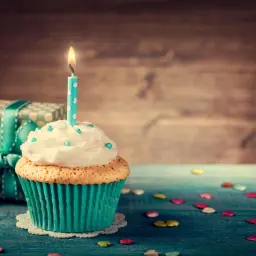 Uroczy cupcake z zapaloną świeczką i prezentem w tle. Idealne з днем народження картинки dla bliskiej osoby.