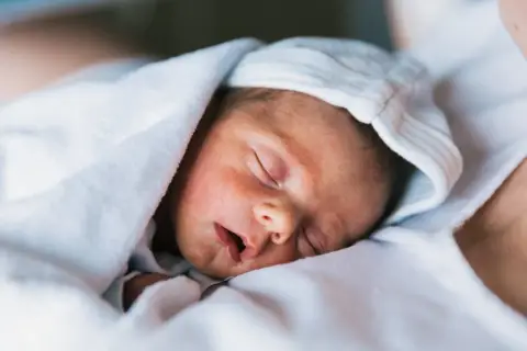 Śpiące niemowlę otulone kocykiem, z czapką na głowie. Może to być mały Ołeksandr lub Sofia, piękne ukraińskie imiona.