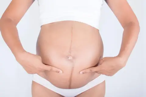 Brzuch kobiety w ciąży z widoczną ciemną linią, linea negra, podkreśloną palcami.
