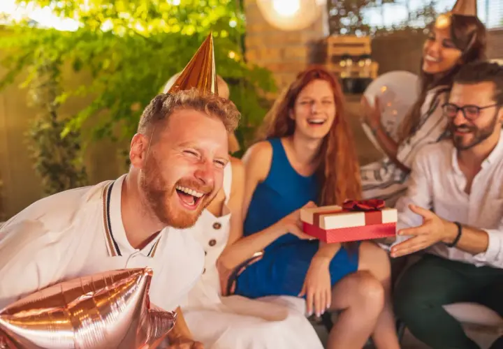 Impreza urodzinowa koleżanki w pełni! Wszyscy się śmieją, a on ma na głowie stożek i trzyma balony.