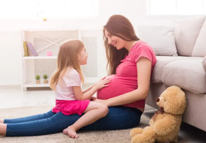 Córka z czułością dotyka brzucha mamy, która wyjaśnia jej, jak wytłumaczyć 10 latkowi skąd się biorą dzieci. Miś czeka na nowego członka rodziny.