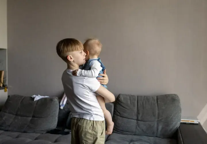 Starszy brat trzyma niemowlę. Zastanawiasz się, od jakiego wieku dziecko może zostać samo w domu?