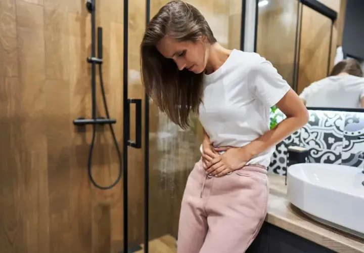 Kobieta w łazience trzyma się za brzuch, zaniepokojona. Czy to plamienie implantacyjne? Zdjęcia mogą pomóc w rozpoznaniu.
