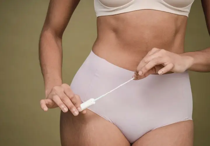 Kobieta trzymająca tampon. Zastanawiasz się, ile może się spóźniać okres? To normalne, że cykl menstruacyjny czasem się waha.