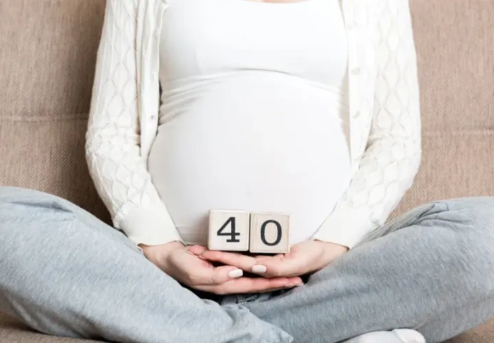Ciąża trwa 40 tygodni. Kobieta w ciąży trzyma w dłoniach kostki z cyframi 4 i 0.