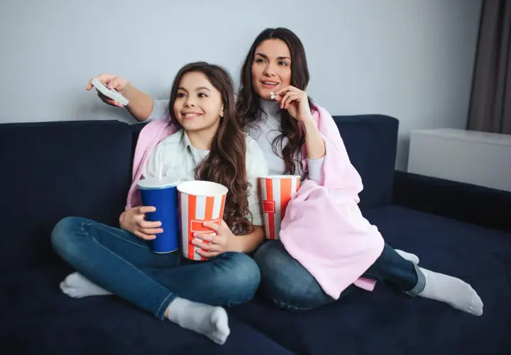 Mama i córka oglądają filmy dla nastolatków, zajadając popcorn i popijając napoje.