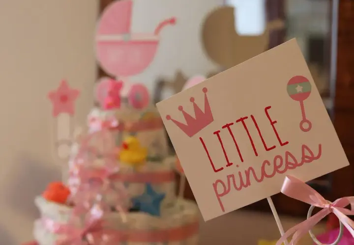 Urocza dekoracja na baby shower z napisem "Little princess", koroną i grzechotką. W tle tort z pieluch i różowa karoca. Prawdziwy mały **gwiazdor**!