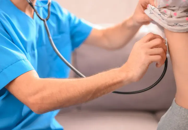 Lekarz osłuchuje klatkę piersiową dziecka, diagnozując zapalenie płuc.