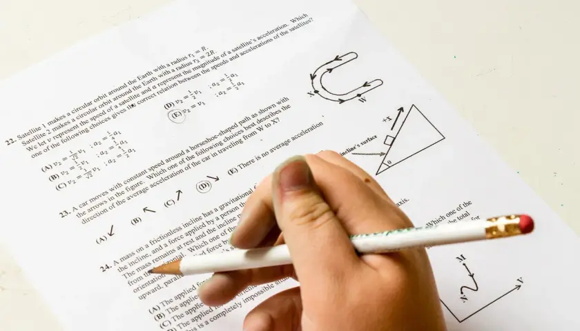 Dłoń z ołówkiem rozwiązuje test z fizyki. Pytanie 22 dotyczy satelitów, a od jakiej średniej jest 5? Odpowiedź D jest zaznaczona.