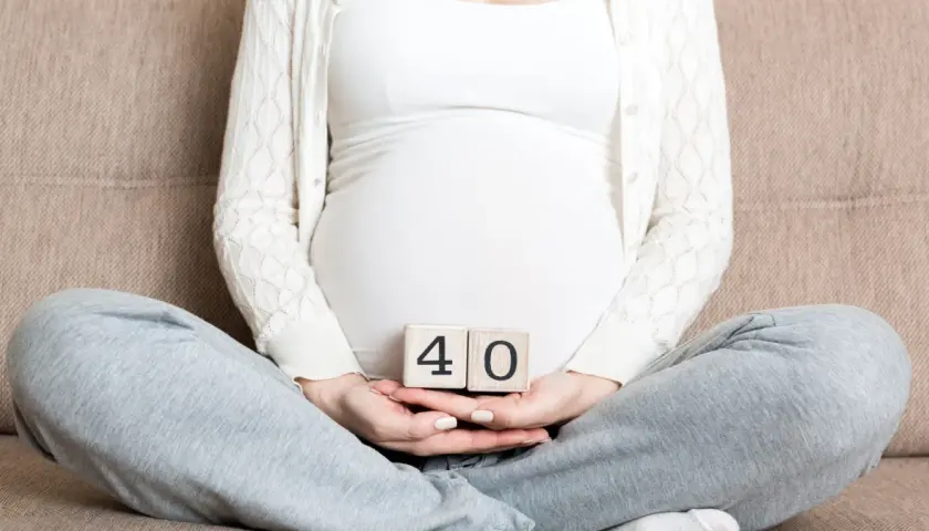 Ciąża trwa 40 tygodni. Kobieta w ciąży trzyma w dłoniach kostki z cyframi 4 i 0.