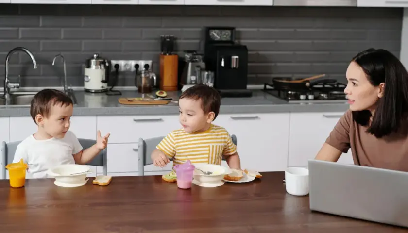 Mama rozmawia z dziećmi przy stole, gdy dziecko zaczyna mówić, gestykulując.