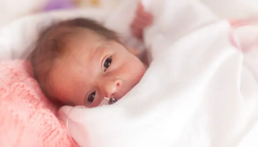 Noworodek z hipotrofią, otulony białym kocykiem, z delikatnym różowym otuleniem po lewej.