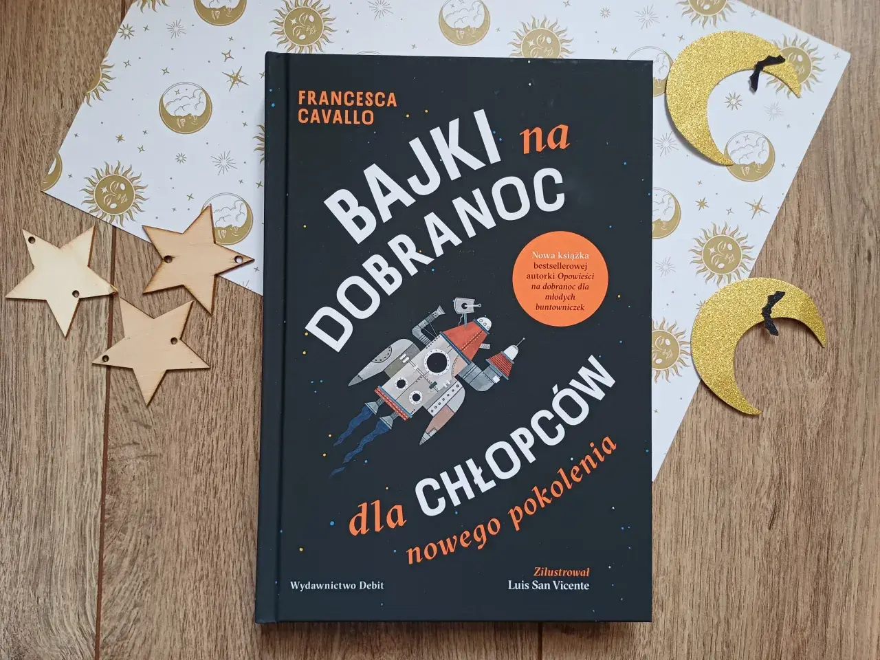 Książka "Bajki na dobranoc dla chłopców nowego pokolenia" z rakietą na okładce, otoczona złotymi gwiazdkami i księżycami.