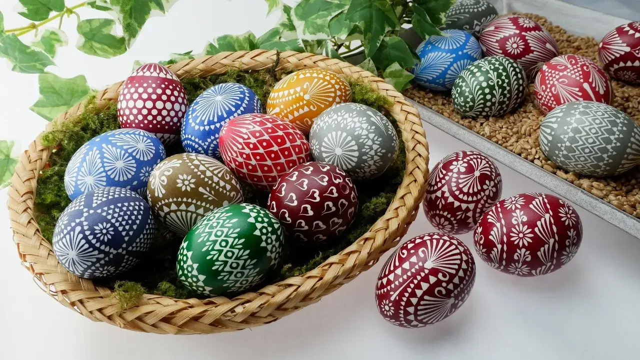Kosz pełen barwnych pisanki kraszanki z tradycyjnymi wzorami. Wśród nich jajka zdobione białymi ornamentami: kwiatami, serduszkami i geometrycznymi motywami.