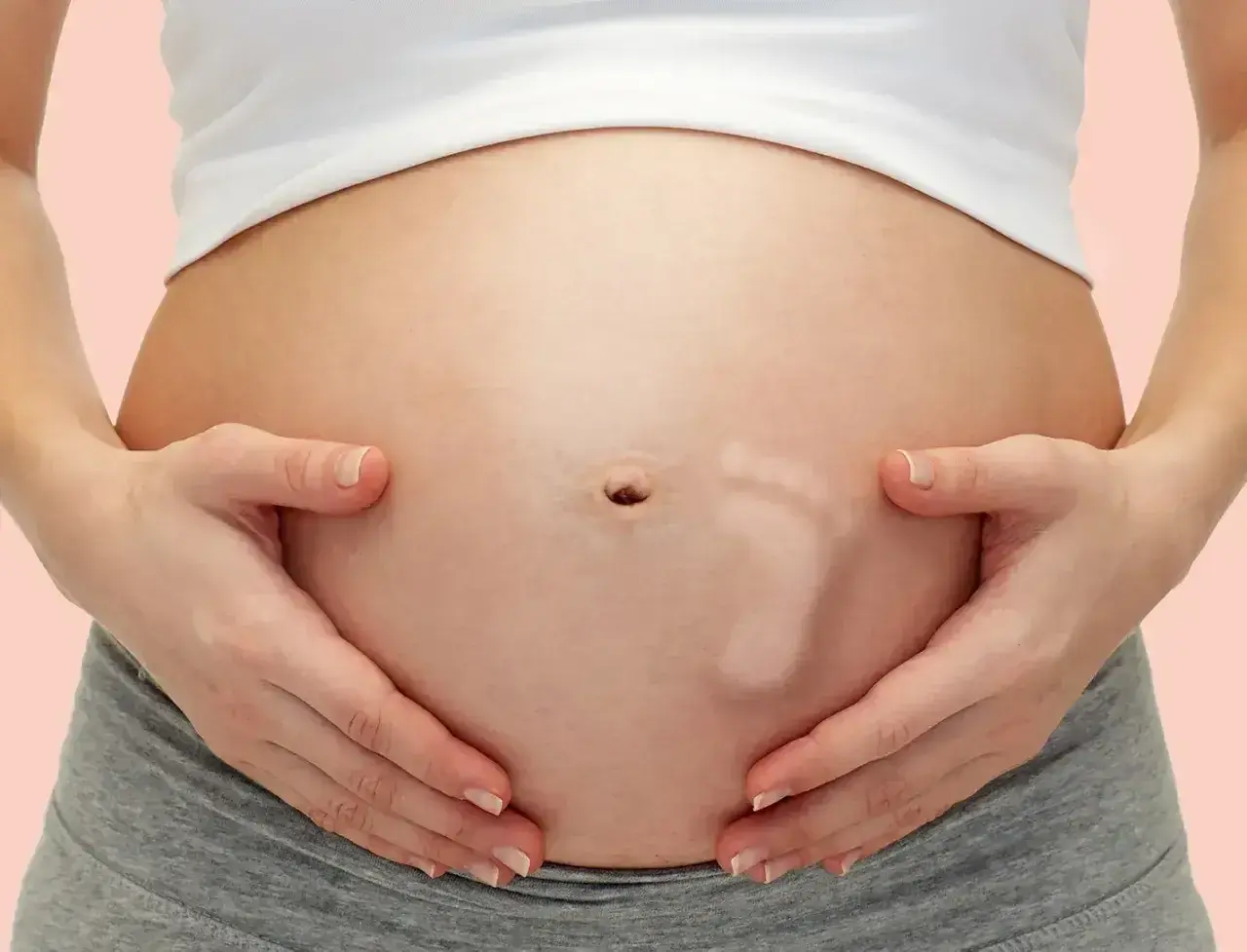 Brzuszek w 30 tygodniu ciąży, z widocznym odciskiem stópki dziecka. Ręce mamy delikatnie obejmują rosnący brzuch.