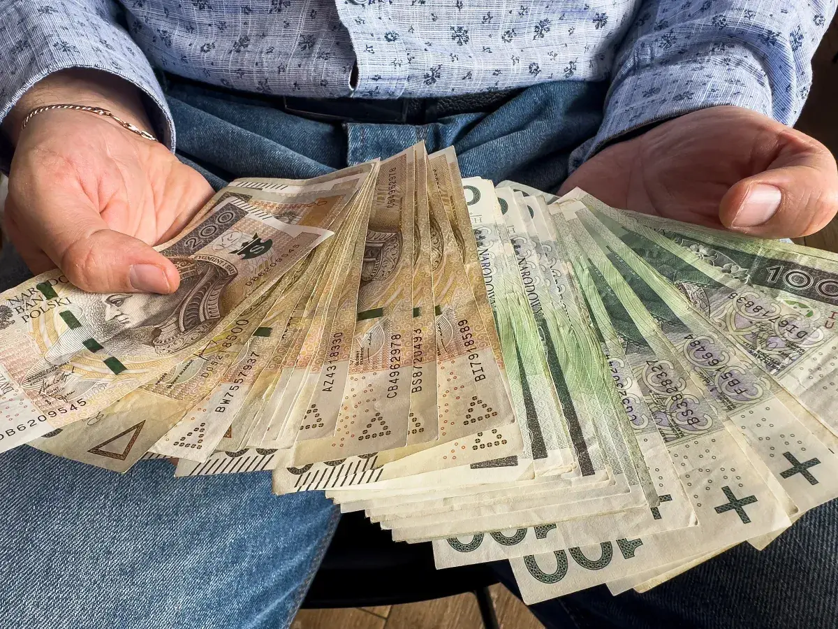 Ręce trzymające plik banknotów. Widać nominały 100, 200, 500 zł. To z pewnością więcej niż 1000 plus.