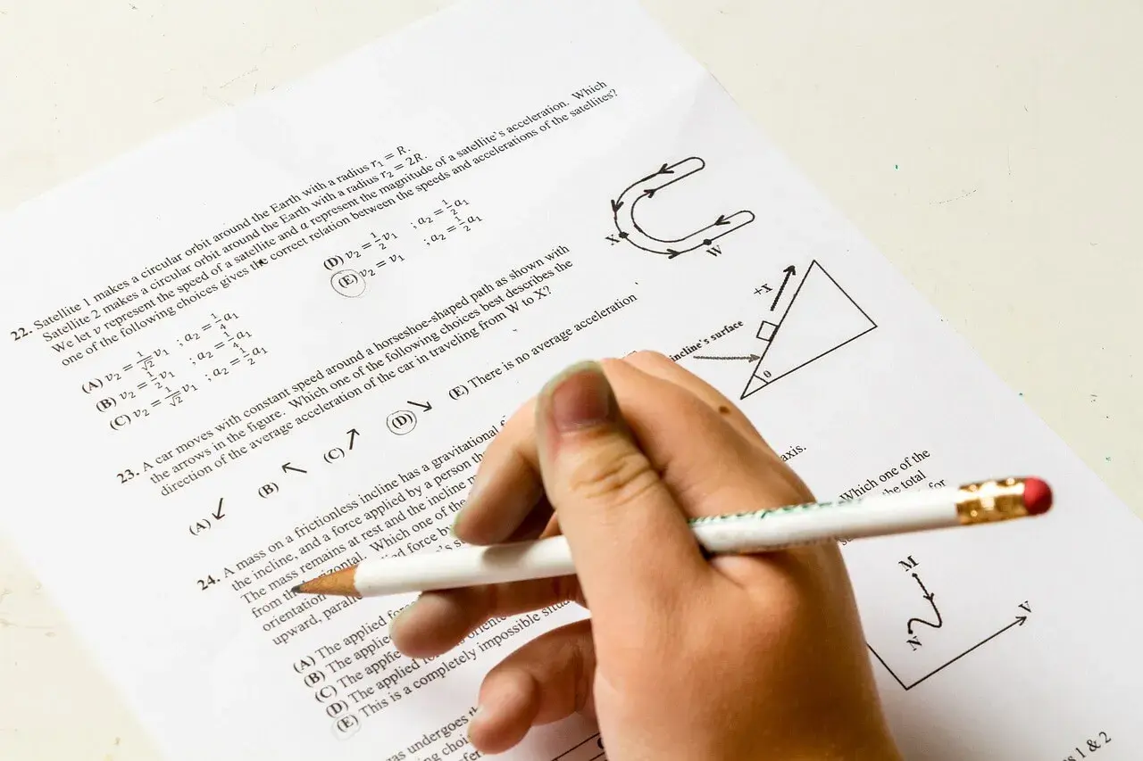 Dłoń z ołówkiem rozwiązuje test z fizyki. Pytanie 22 dotyczy satelitów, a od jakiej średniej jest 5? Odpowiedź D jest zaznaczona.